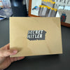 A brown envelope with the text SECRET HITLER printed on it, held by a hand.