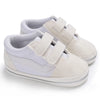 A pair of light gray canvas baby sneakers with white laces and soft beige accents.