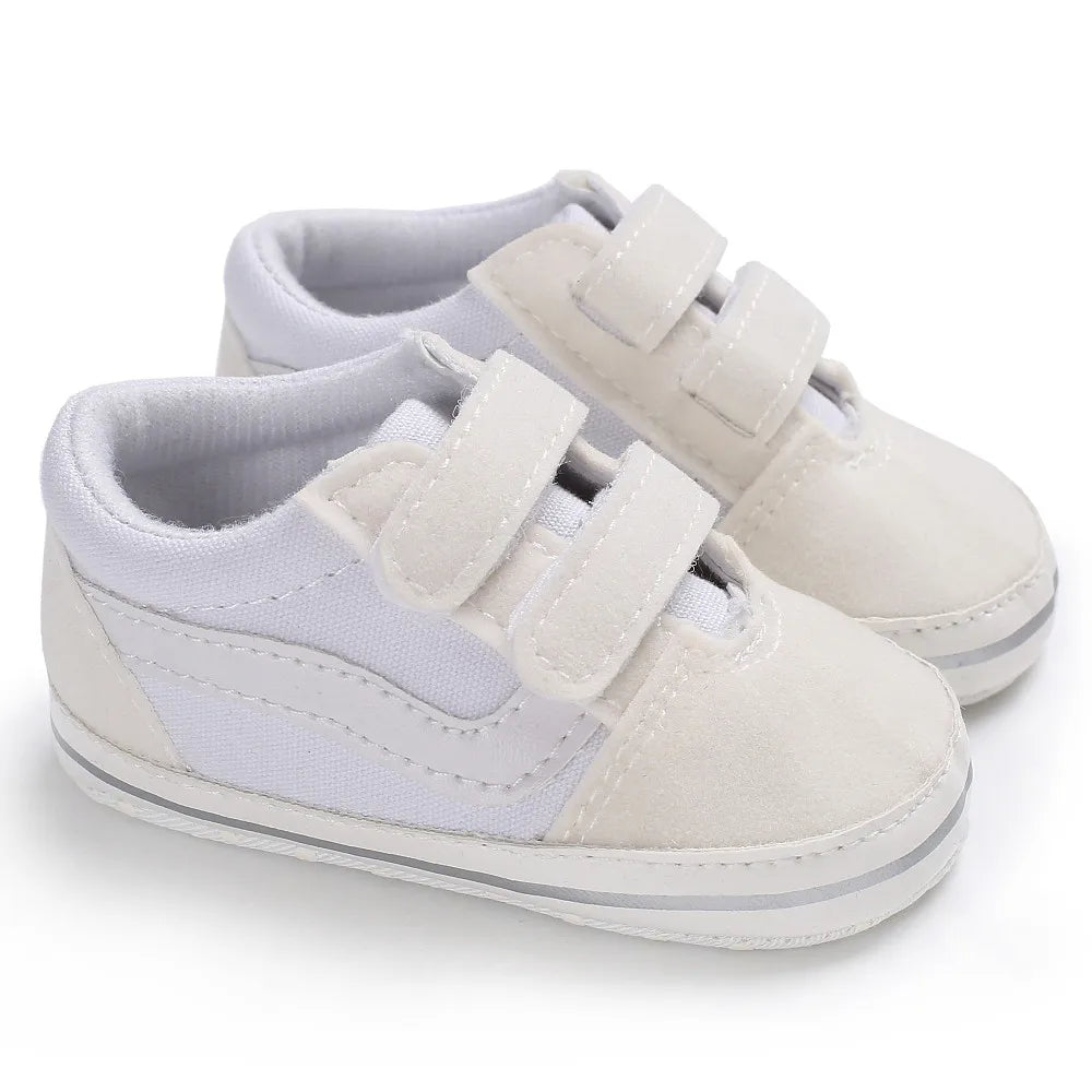 A pair of light gray canvas baby sneakers with white laces and soft beige accents.