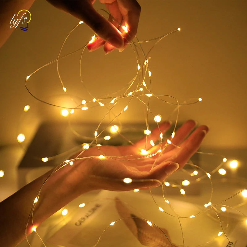 A hand is holding and manipulating thin fairy lights that are glowing brightly against a dark background.