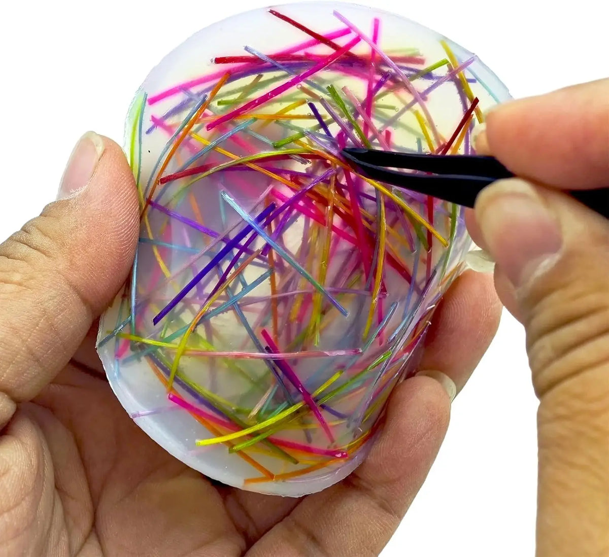 A hand holds a silicone fidget picking pad filled with colorful wires and a black tweezer for stress relief.