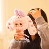 A person is holding a pink fluffy collectible figure with purple ears and a face, against a light background.