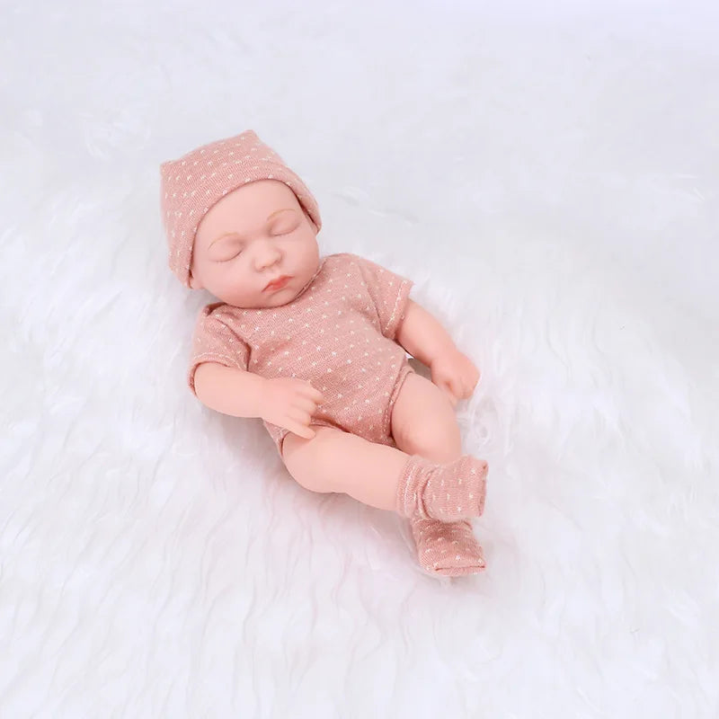 A realistic soft vinyl baby doll wearing a matching pink outfit and cap, lying on a white surface.