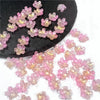 Pink and yellow sakura flower crystal glass beads scattered on a dark surface