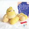A yellow crocheted bird toy next to yarn and a purple DIY crochet kit bag.