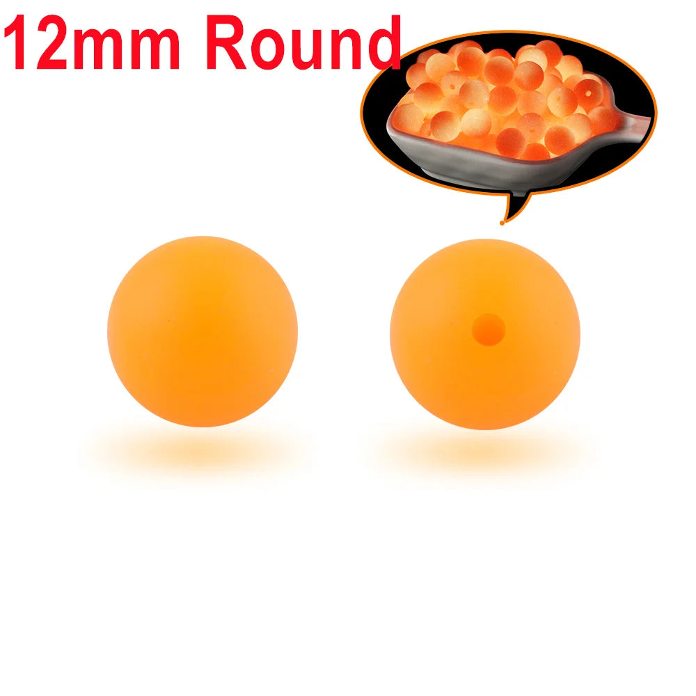 Two round orange silicone beads, one solid and one hollow, shown next to a bowl of similar beads.