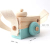 A wooden camera teether toy with a light blue body and beige fabric strap.