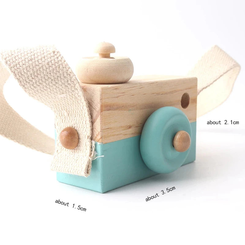 A wooden camera teether toy with a light blue body and beige fabric strap.