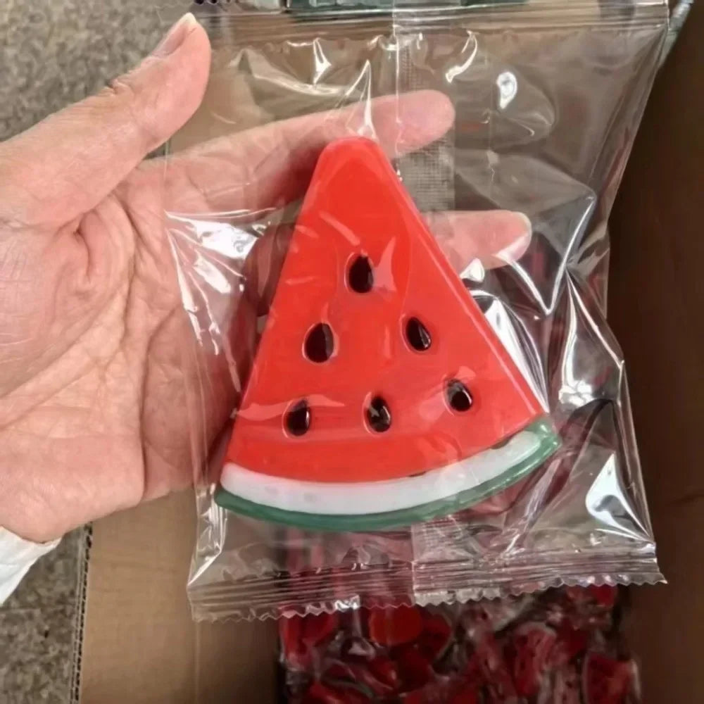 An oversized red watermelon slice stress relief toy is visible inside a clear plastic bag being held by a hand.