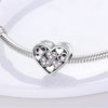 A sterling silver heart charm bead with small pink stones is displayed on a white surface.