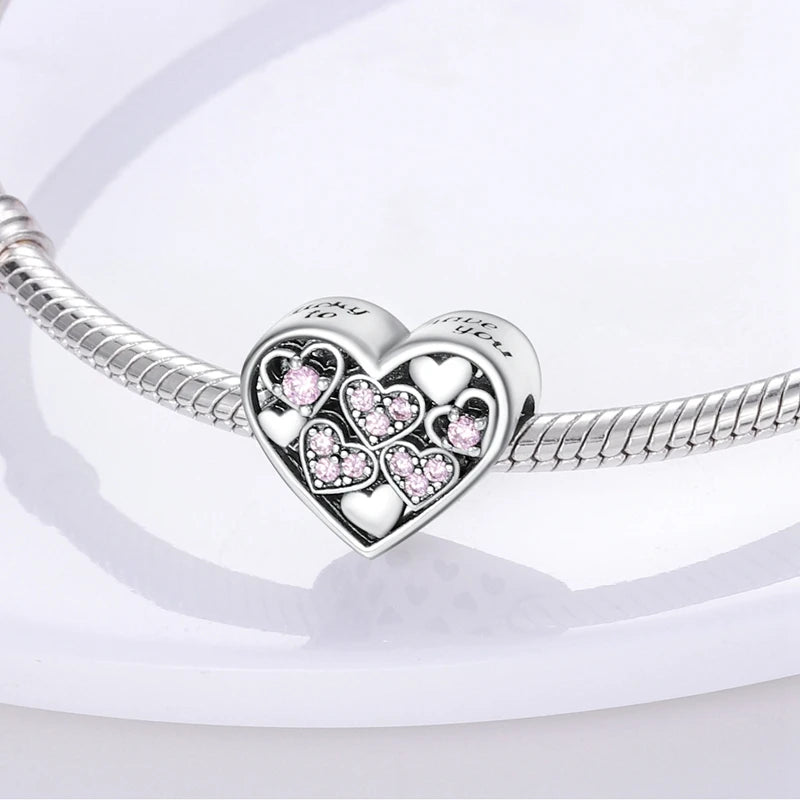 A sterling silver heart charm bead with small pink stones is displayed on a white surface.