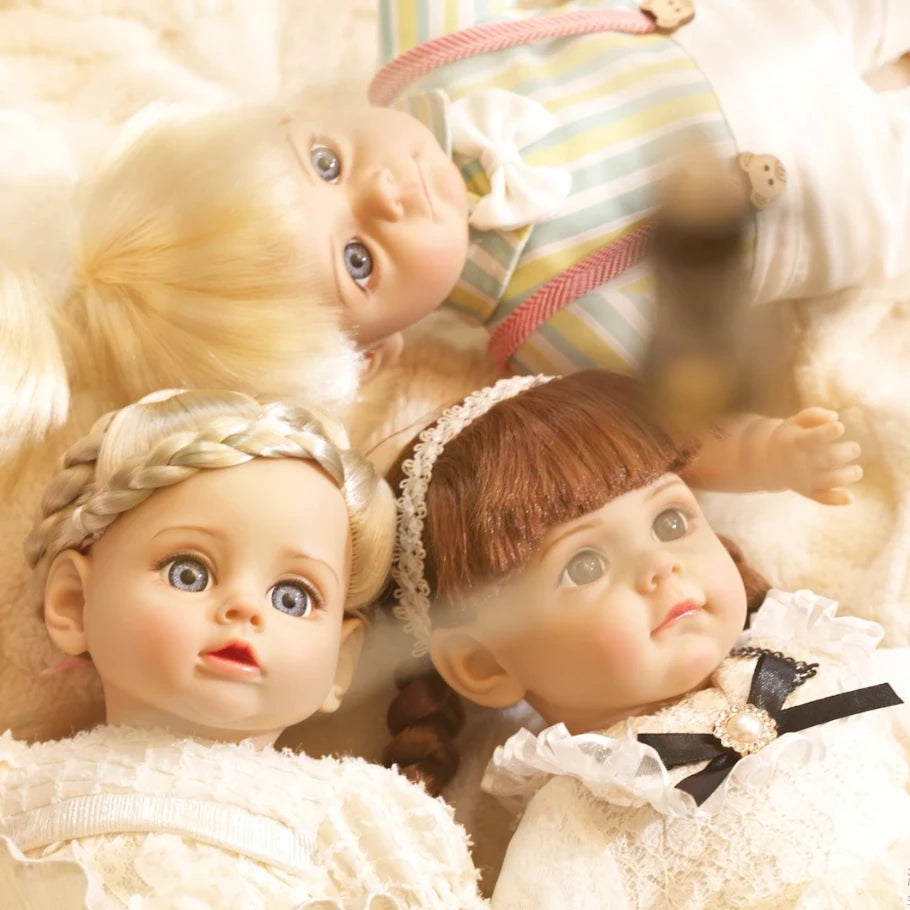 A close-up of a lifelike 14-inch reborn baby doll with blonde hair and blue eyes wearing a white outfit.