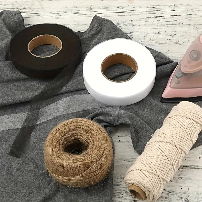 Rollen von doppelseitigem Eisen-auf-Stoff-Verstärkungsband in Schwarz, Weiß und Naturbeige auf grauem Stoff.