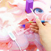 A hand uses an electric diamond painting pen kit to apply colored dots onto a pink background.