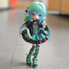 A female BJD doll with teal hair and blue eyes wearing a dark outfit and green accents.