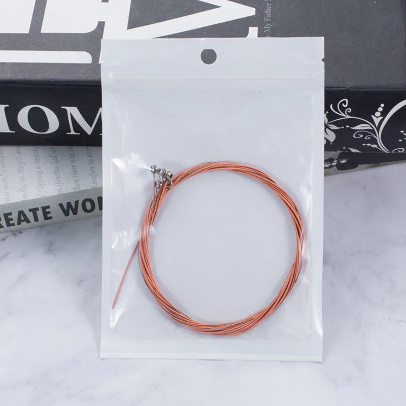A spool of copper-colored acoustic guitar strings is sealed in a clear plastic pouch with a string changer tool.