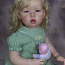 A realistic reborn baby doll with soft cloth body, featuring blonde hair and a green dress.