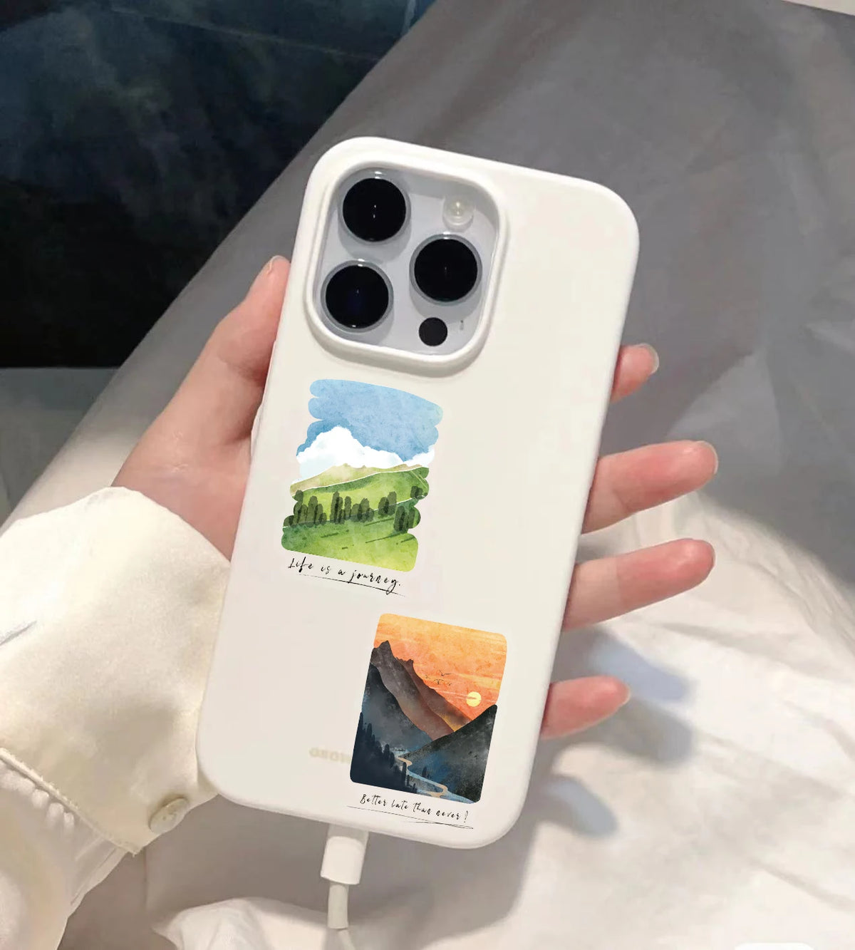 A white smartphone features a decorative sticker pack depicting a landscape with mountains and the sea.