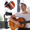 A man holds an acoustic guitar while a black phone holder is mounted on a stand.