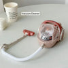 A pink vacuum cleaner with a hose and cleaning head is shown next to a white cup.