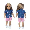 A doll wearing a blue shirt and pink shorts with white shoes.