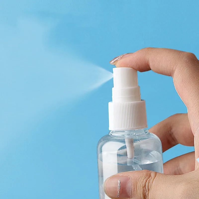 A hand is spraying a fine mist from a white pump bottle against a light blue background.