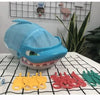 A blue shark-shaped toy is displayed with various yellow, red, and green plastic shark teeth accessories on a white surface.