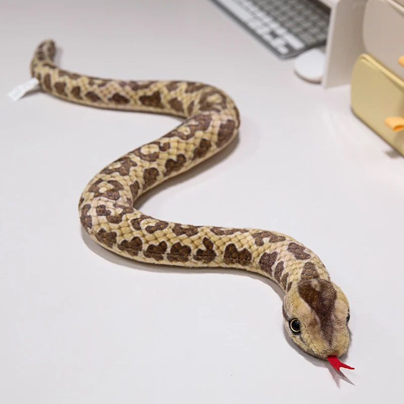 A lifelike simulation snake plush toy with mottled brown and tan patterning is coiled on a white surface.