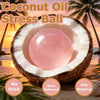 A pink coconut oil stress ball inside a halved coconut shell on a sandy beach.