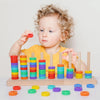 A toddler is stacking colorful wooden rings in a tower on a light wooden board.