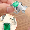 A hand is using a professional bezel setting pusher tool with a silver and green gemstone to set a ring.