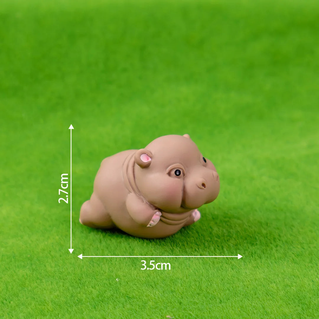 A small, light brown resin figurine of a hippo in a resting pose, photographed on green grass.