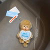 A cute brown Monchhichi plush toy with a heart-shaped tag that reads We are sweet friends