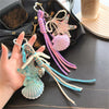 A hand holds a set of beaded keychains featuring starfish and seashell charms in shades of purple, pink, and blue.