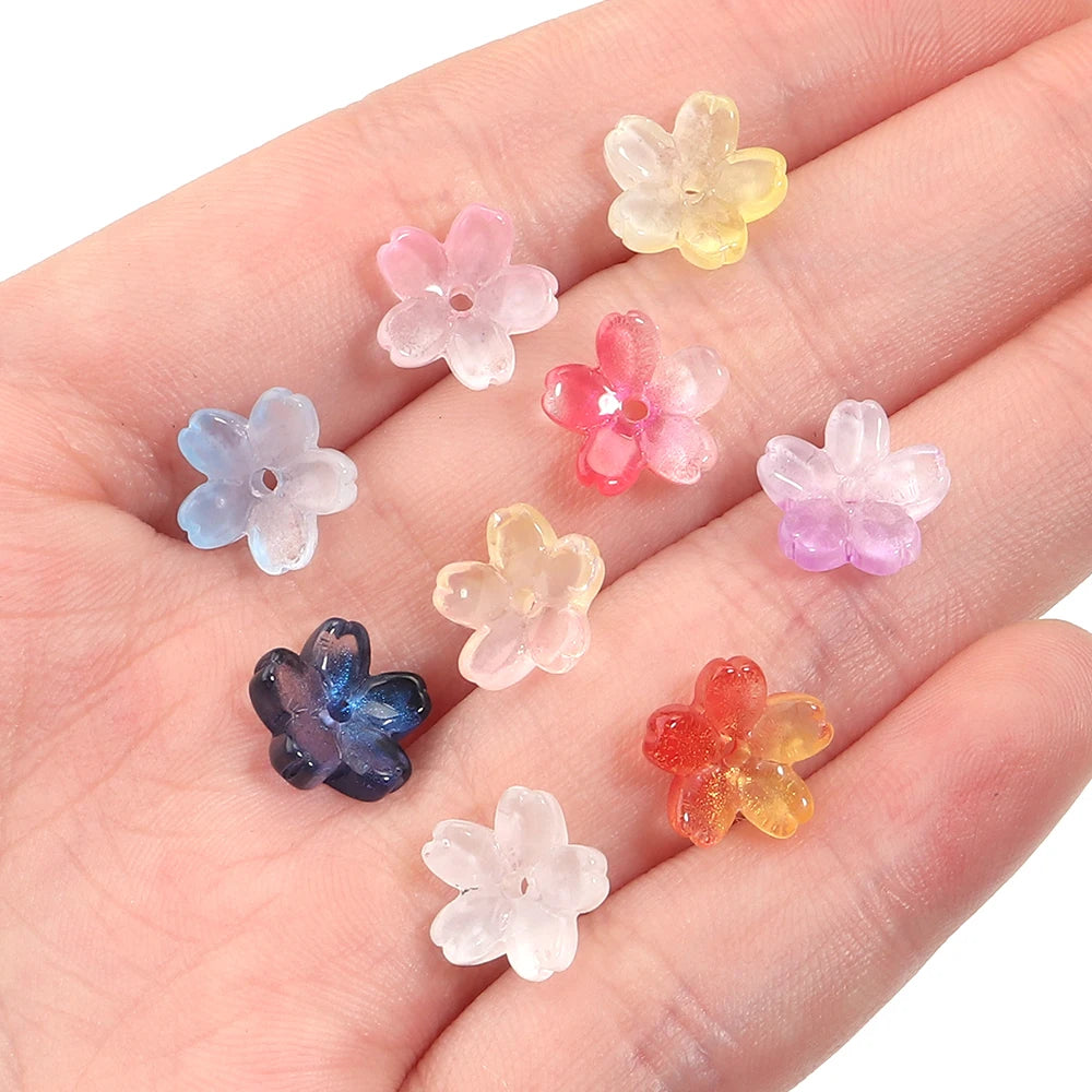 A hand holds a set of 50 glass beads shaped like cherry blossom flowers in various pastel colors.