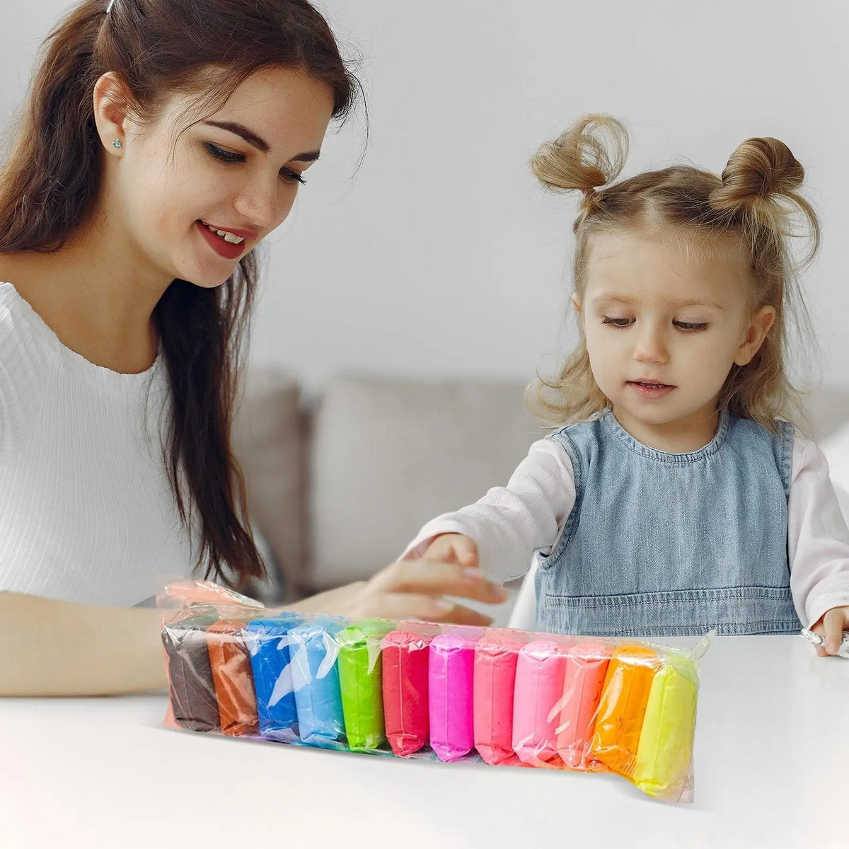 A young girl is modeling vibrant air dry clay with tools on a white table, supervised by an adult.