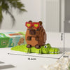 A wooden building block set shaped like a capybara, featuring brown body and red eyes, resting on green foliage.