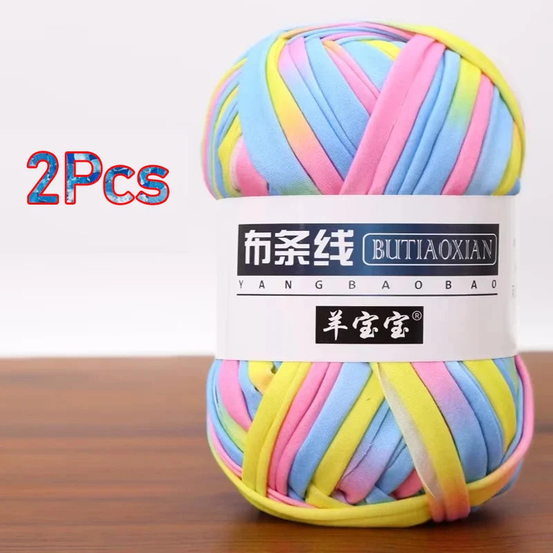 A skein of multi-colored soft chunky t-shirt yarn in pink, blue, and yellow is shown on a wooden surface.