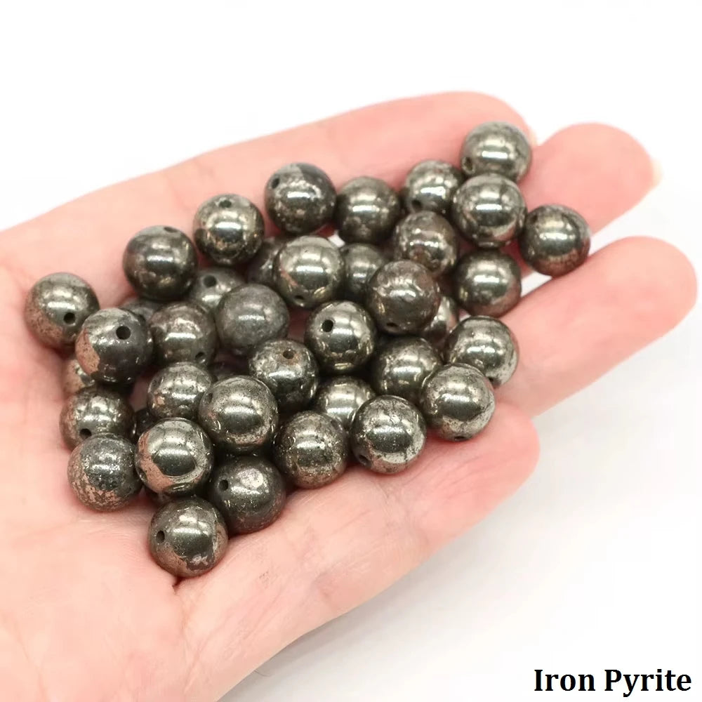 A handful of dark, round iron pyrite beads resting on a person's palm.