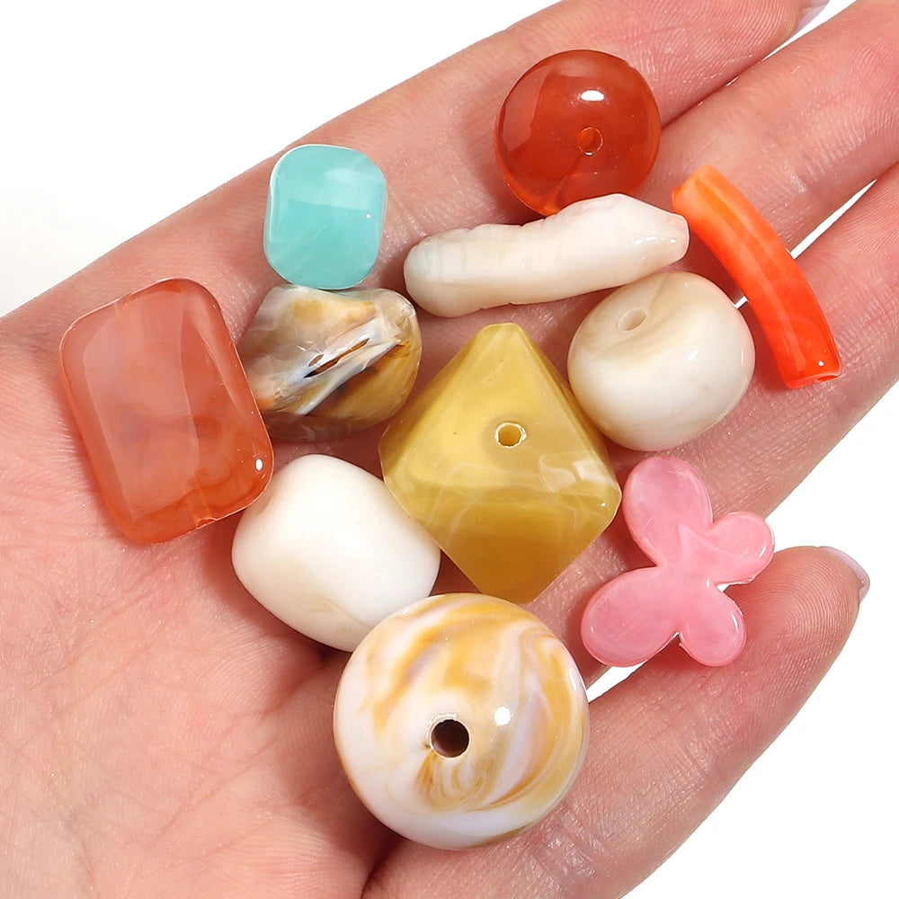 A hand holds a collection of colorful, translucent acrylic beads in various shapes and colors for jewelry making.