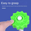 A hand is grasping a bright green spin tower toy with a white ball on top, demonstrating its easy to grasp design.