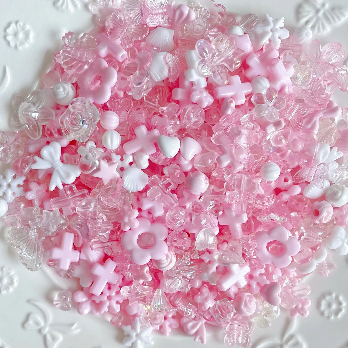 A pile of pink and white acrylic bow and flower beads for DIY jewelry making