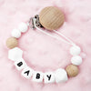 A bracelet made of white and natural wood silicone beads attached to a clip, spelling out BABY.