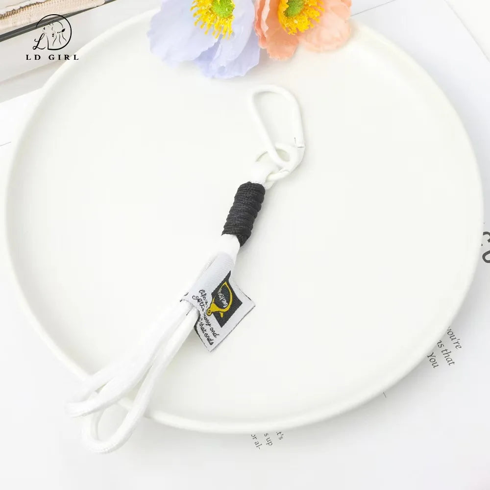 A white plate holds a soft bunny plush keychain with a bow charm and a black cord.