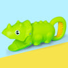 A bright green plastic dinosaur toy with a yellow handle and claw features, lying on a yellow surface.