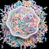 A white dish filled with colorful polymer clay sprinkles mixed with small plastic figures, scattered on a black background.