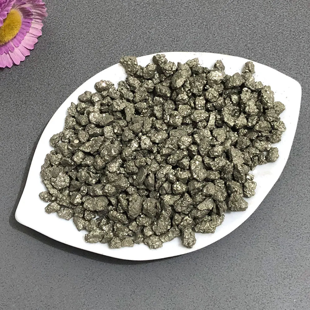 A pile of dark metallic natural crystal chips, including chalcopyrite and pyrite mineral decor, on a white plate.