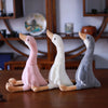 Three plush toys of long-necked geese in pink, white, and gray colors resting on a wooden surface.