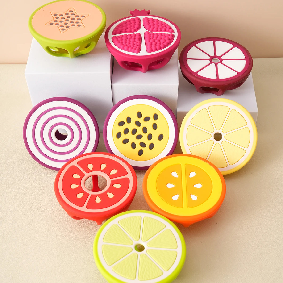 A set of silicone baby teethers shaped like various fruits and vegetables in pink, yellow, and orange colors.
