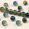 A collection of blue and gold gradient crystal glass beads with a crackle finish scattered on a white textured surface.